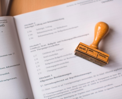 Das Bild zeigt ein offizielles Dokument mit einem Stempel, der darauf liegt. Auf dem Stempel steht das Wort "geprüft."