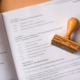 Das Bild zeigt ein offizielles Dokument mit einem Stempel, der darauf liegt. Auf dem Stempel steht das Wort "geprüft."